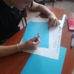 Uczeń w trakcie pracy na materiałami na niebieskich kartkach papieru.
