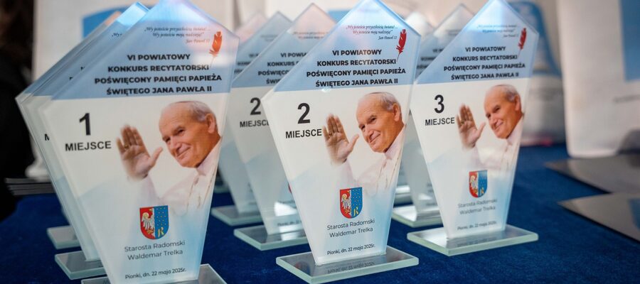 Szklane trofea ustawione w rzędach na granatowym obrusie. Każde trofeum przedstawia zdjęcie uśmiechniętego papieża Jana Pawła II z uniesioną ręką. Nagrody są opisane jako pamiątki z VI Powiatowego Konkursu Recytatorskiego poświęconego pamięci papieża. Na górze trofeum znajduje się cytat Jana Pawła II: „Wy jesteście przyszłością świata… Wy jesteście moją nadzieją!”.