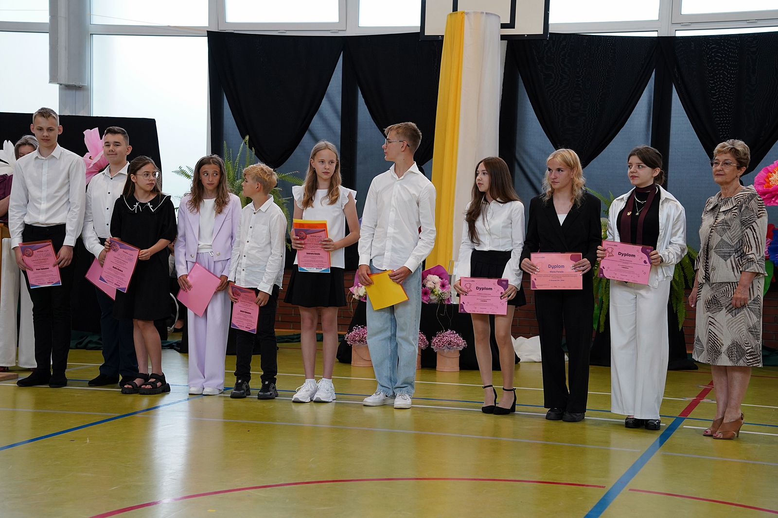 Zdjęcie grupowe nagrodzonych uczniów. W dłoniach dyplomy w kolorze różowym. Jeden uczeń trzyma dyplom w kolorze żółtym