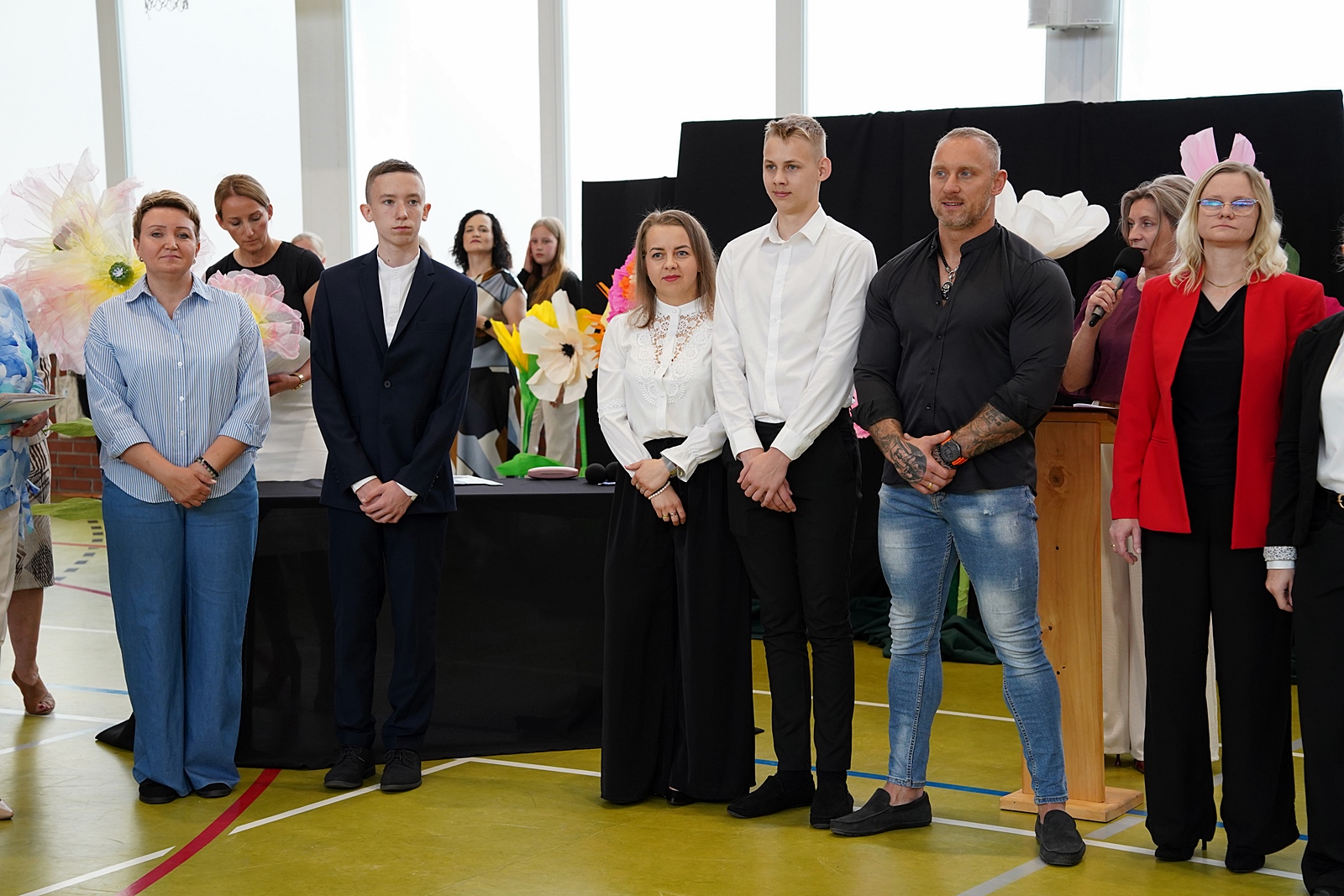 Grupa rodziców z dziećmi w oczekiwaniu na wręczenie gratulacji przez dyrekcję szkoły.