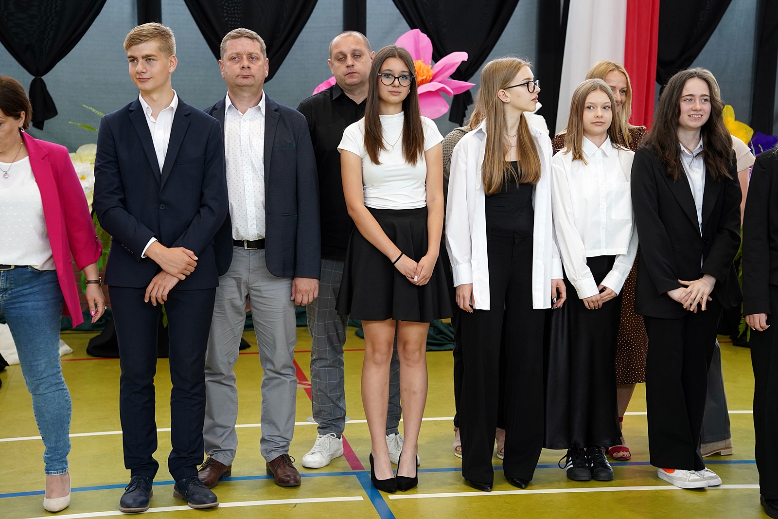 Grupa rodziców z dziećmi w oczekiwaniu na wręczenie gratulacji przez dyrekcję szkoły.