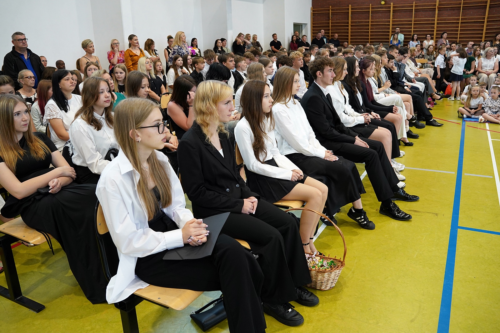 Uczniowie siedzący na krzesłach słuchają przemówienia.