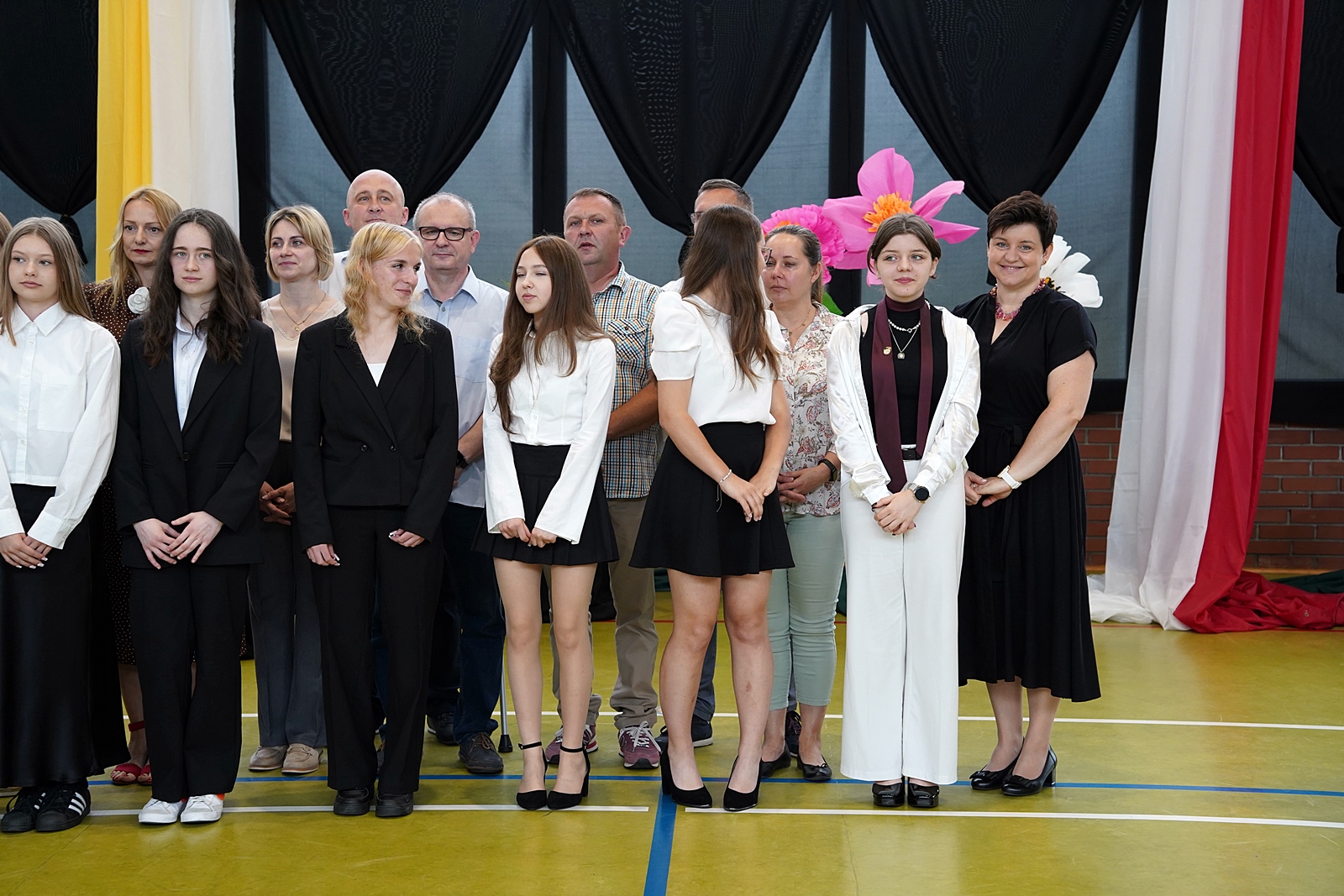 Grupa rodziców z dziećmi w oczekiwaniu na wręczenie gratulacji przez dyrekcję szkoły.