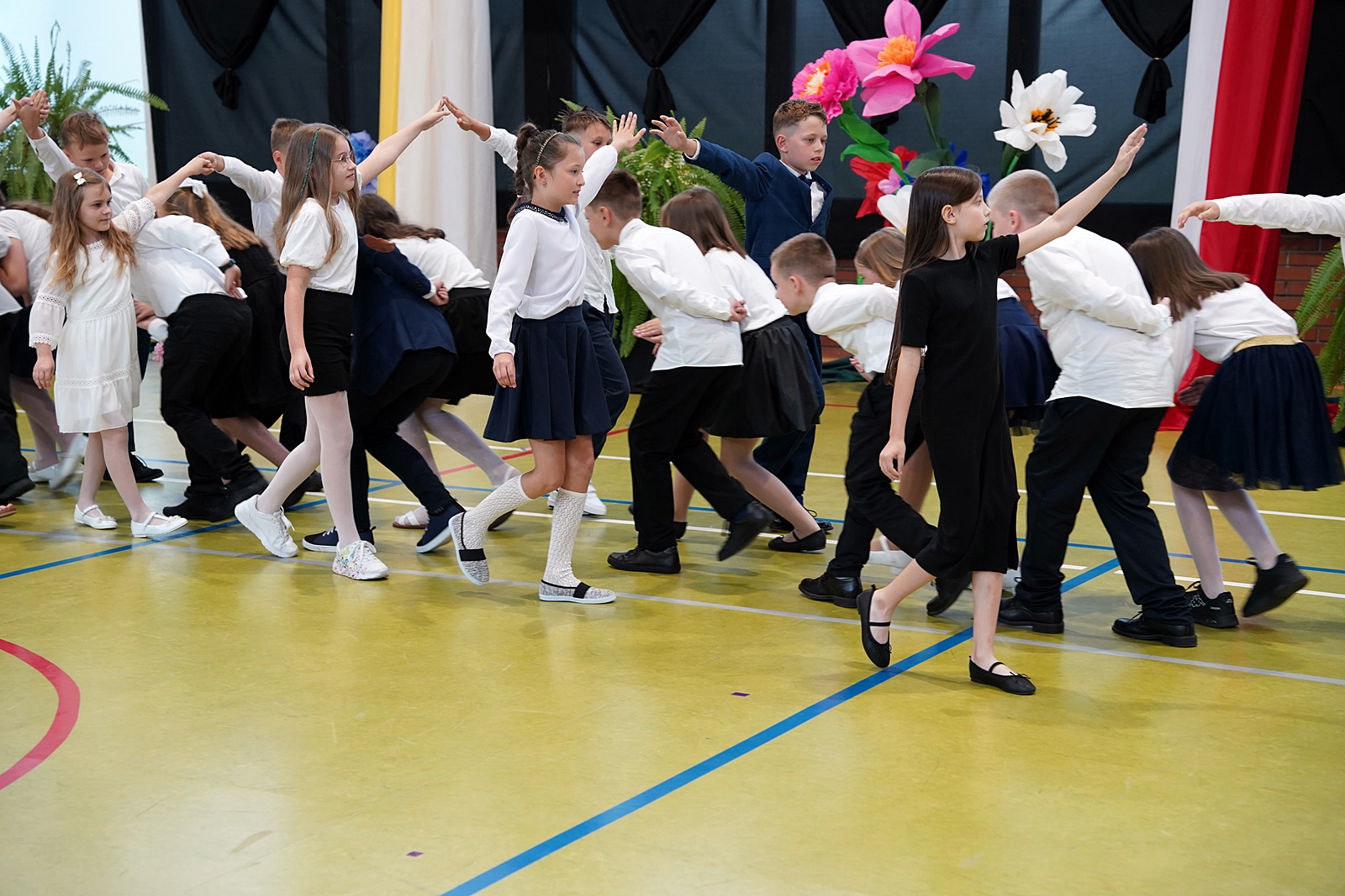 Grupa uczniów klas młodszych tańczy poloneza.