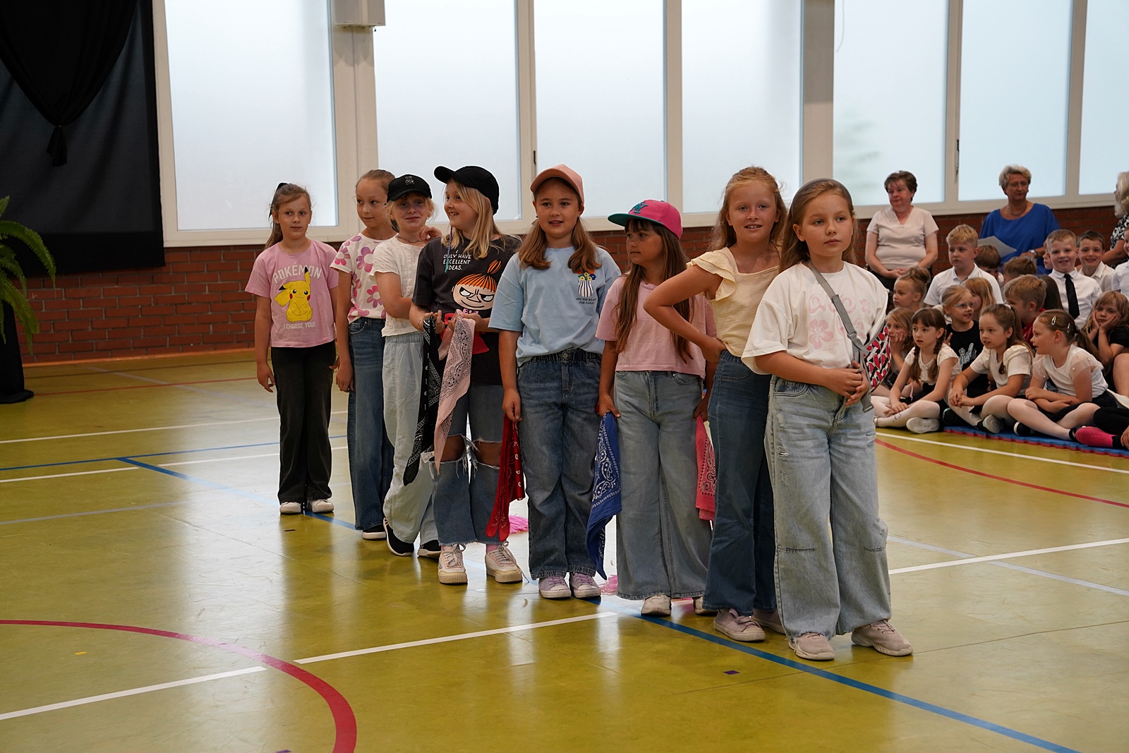 Grupa uczniów i uczennic rzędzie podczas przygotowań do występu. W dłoniach chusty, na głowach czapki bejsbolówki.