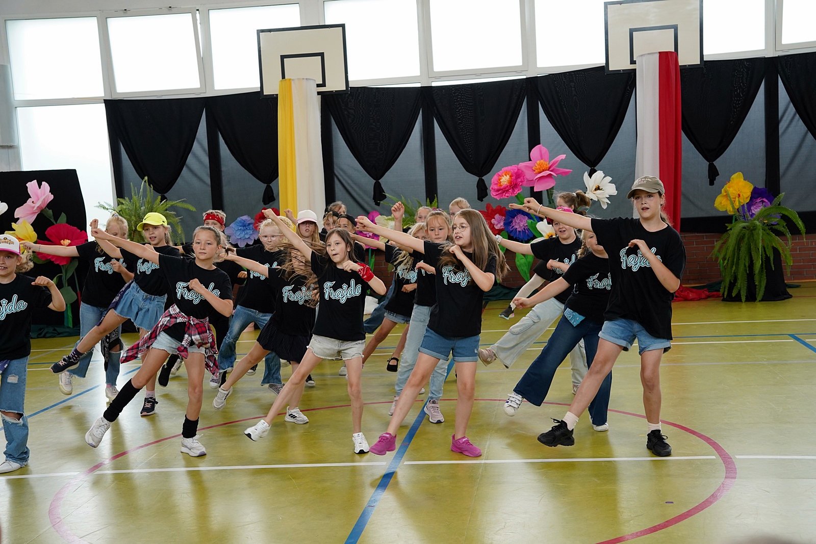 Grupa "Frajda" podczas występu. Wszyscy stoją na lewej nodze. Prawa noga lekko uniesiona nad podłogą. Prawa ręka skierowana na ukos do góry.