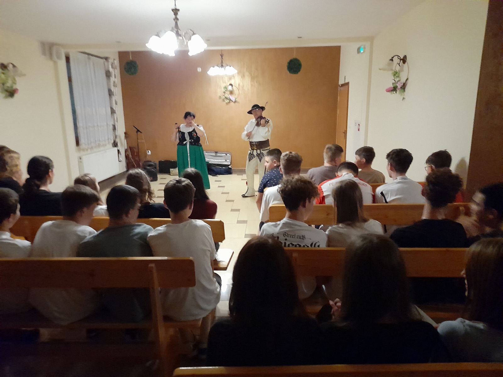 Góral i góralka występują przez publicznością. Zdjęcie zza pleców grypy uczniów.