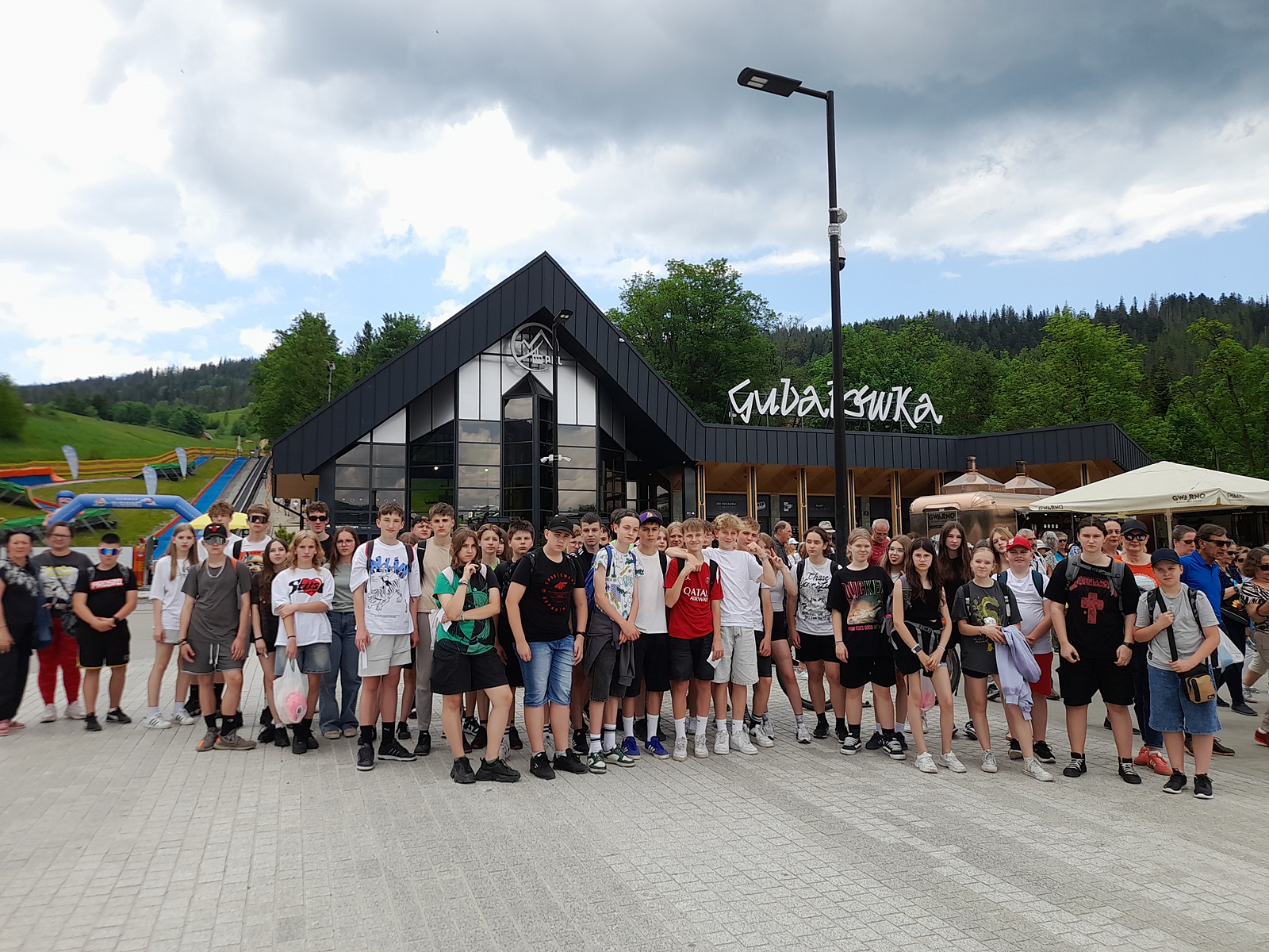 Zdjęcie grupowe pod wyciągiem Gubałówka. W tle budynek z napisem.