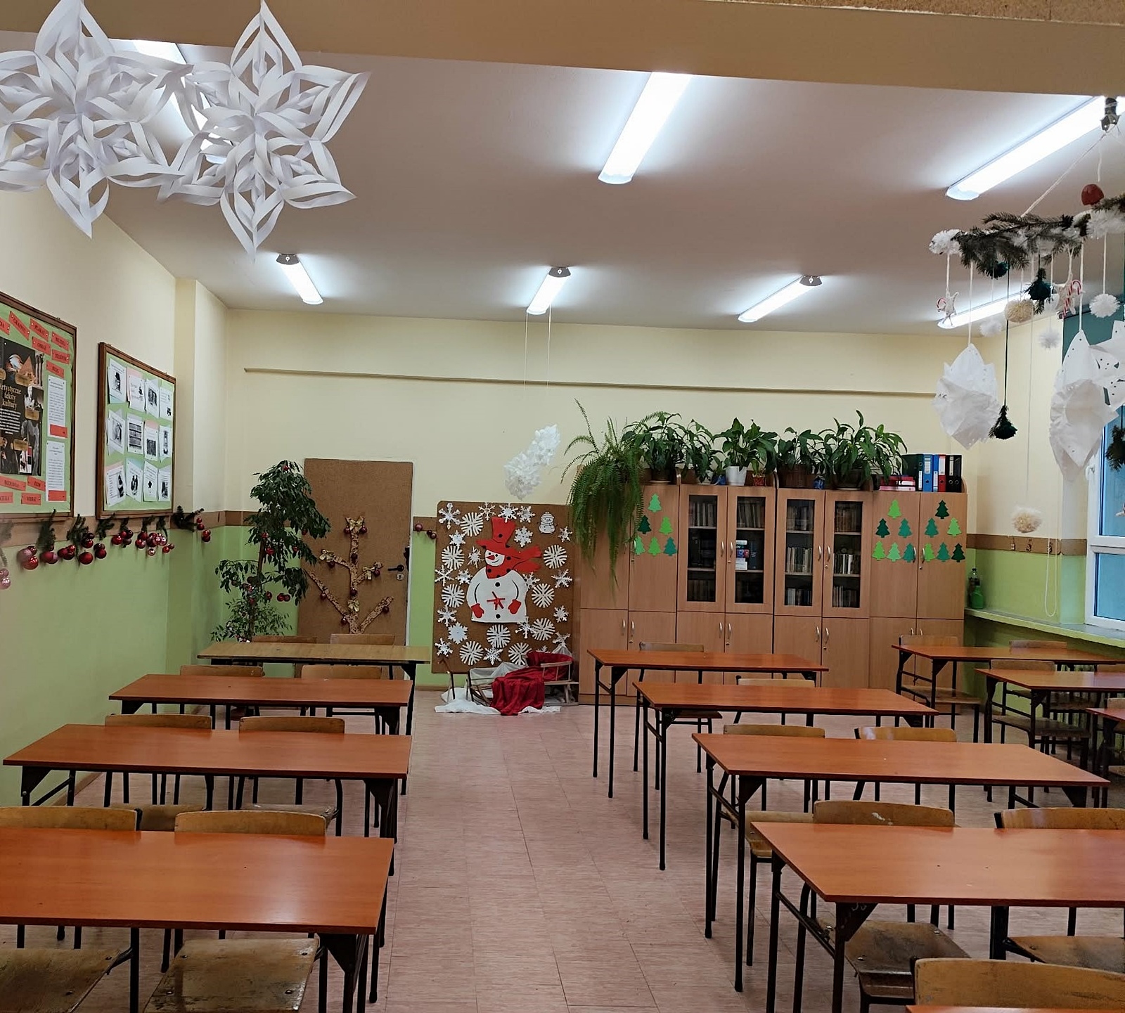 Udekorowana sala lekcyjna: wiszące białe gwiazdki - płatki śniegu, tablica korkowa z dużą sylwetką bałwana w czerwonym kapeluszu i szaliku.