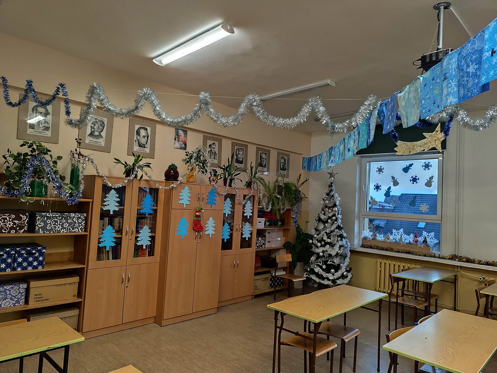 Świątecznie udekorowana sala lekcyjna - choinka, srebrne łańcuchy pod sufitem, papierowe choinki na meblach.
