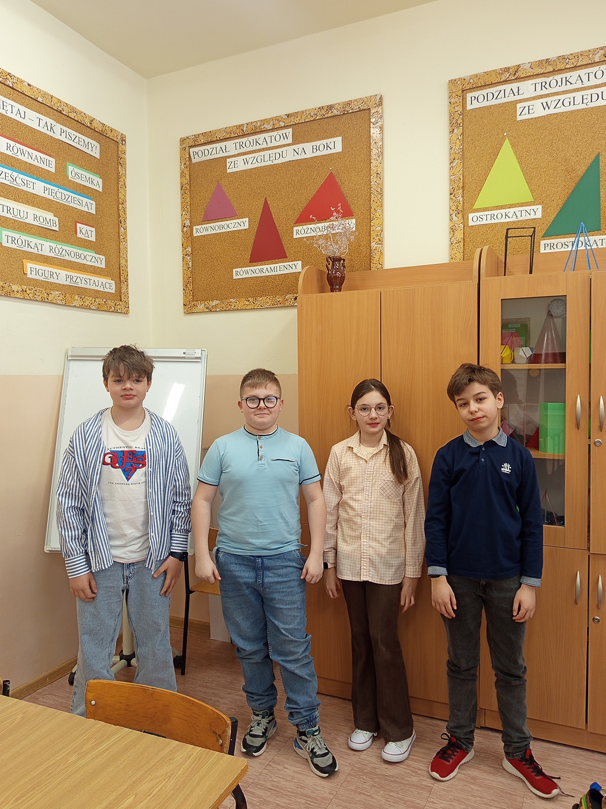 Czworo uśmiechniętych uczniów pozujących w kolorowych koszulach.
