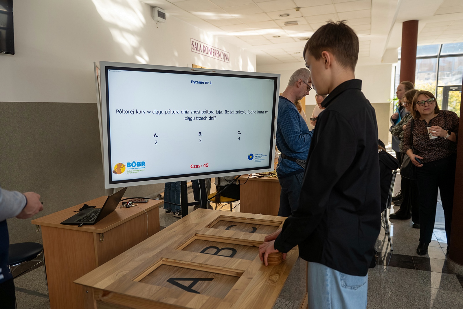 Uczeń przed dużym dużym monitorem, na którym wyświetlane jest zadanie konkursowe.
