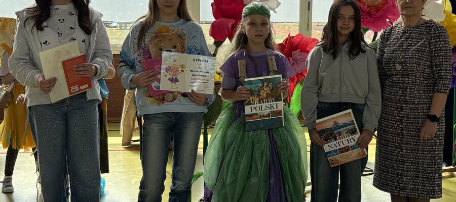Cztery dziewczynki w wieku szkolnym i z prawej strony dorosła kobieta. Dziewczynki trzymają dyplomy oraz nagrody książkowe.