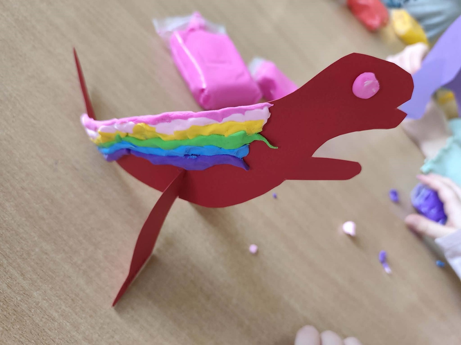Wycięty z papieru czaerwony dinozaur, ozdobiony przez dzieci kolorowymi kropkami z piankoliny.