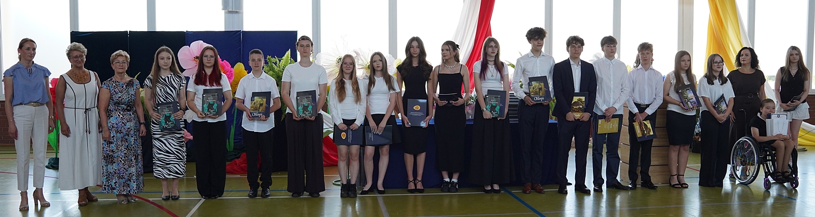 Grupa wyróżnionych uczniów stojąca w rzędzie z osobami dorosłymi (dyrekcja szkoły). Uczniowie trzymają w rękach pamiątkowe albumy.