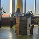 Kobieta stojąca (przemawiająca) za mównicą z tabliczką "PSP nr 5 w Pionkach". Ma ciemne długie włosy, okulary; ubrana w białą bluzkę i ciemne spodnie.